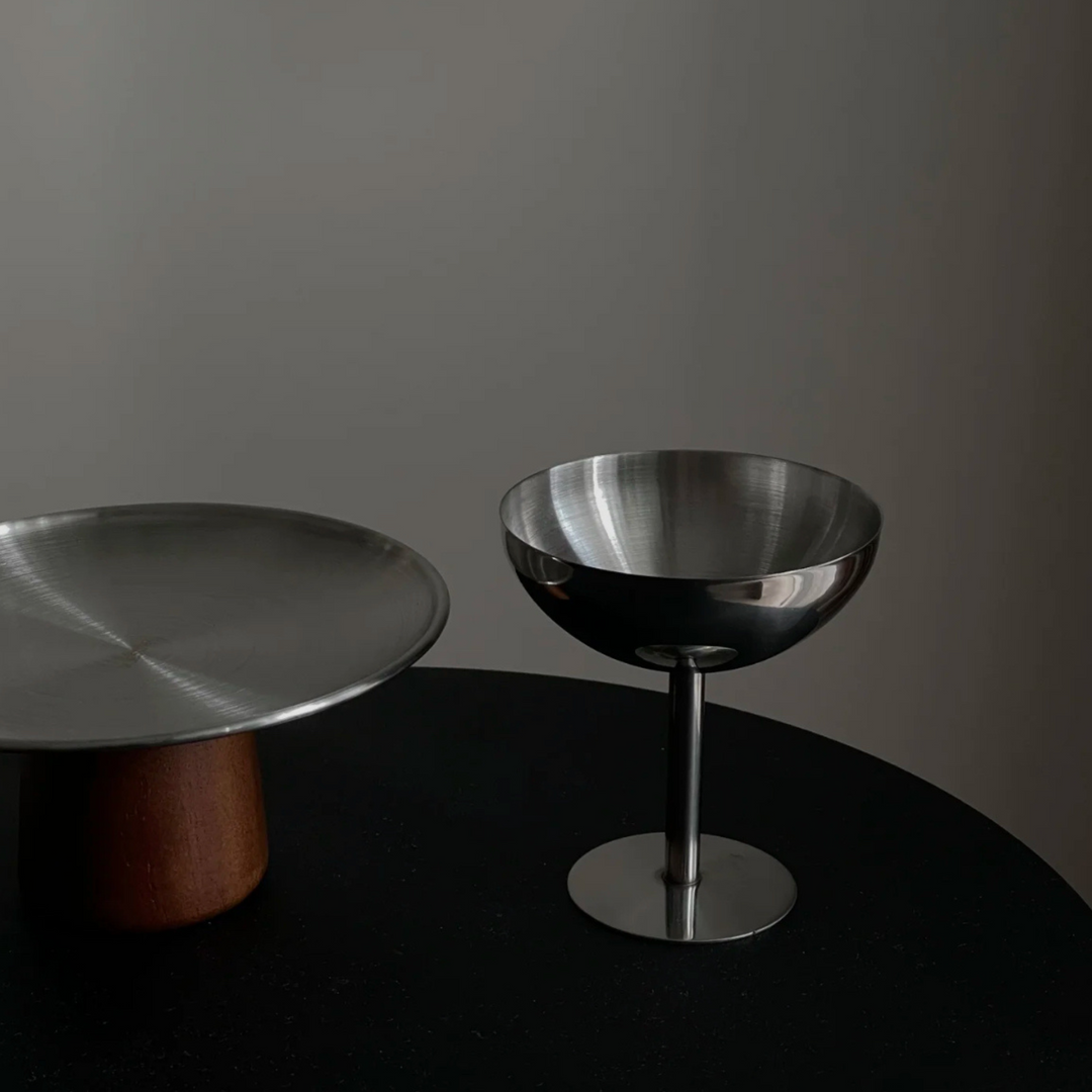 Hand-polished stainless steel coupe placed on a dark tabletop, offering sleek design for minimalist decor.