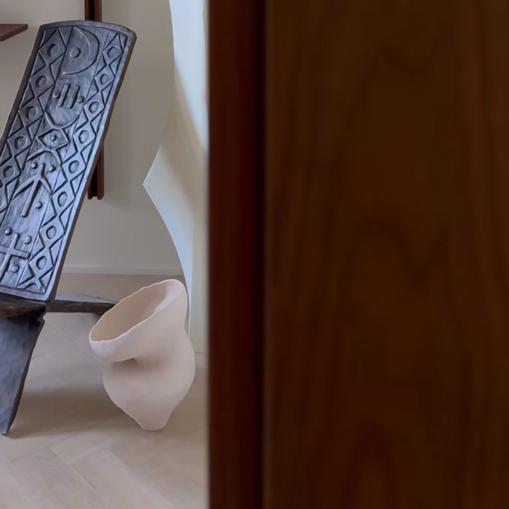 Handmade ceramic vase placed beside a modern accent chair.