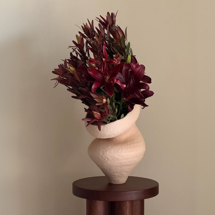 Handmade ceramic vase filled with rich burgundy florals on pedestal.