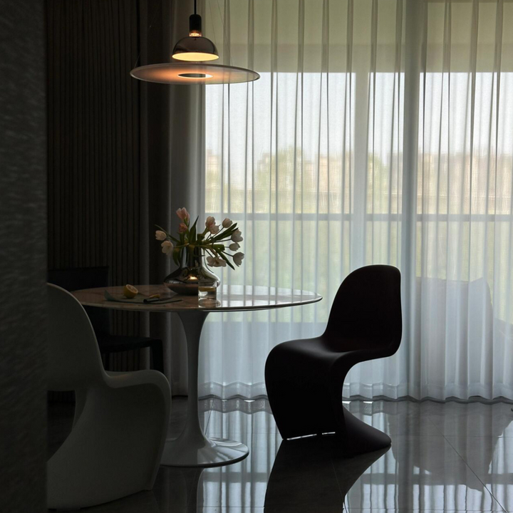 Intimate dining area with chrome pendant light, round table, and sheer curtains