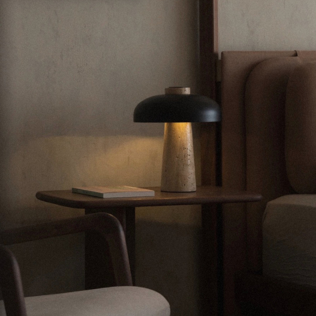 table lamp featuring an iron shade and travertine base placed beside a lounge chair.