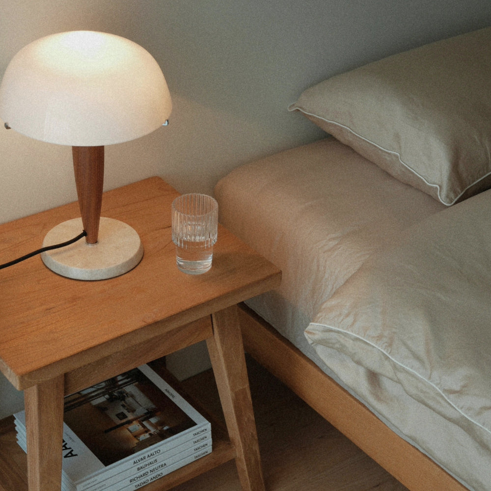 placed on a wooden nightstand a table lamp with marble base and glass dome casts warm ambient light.