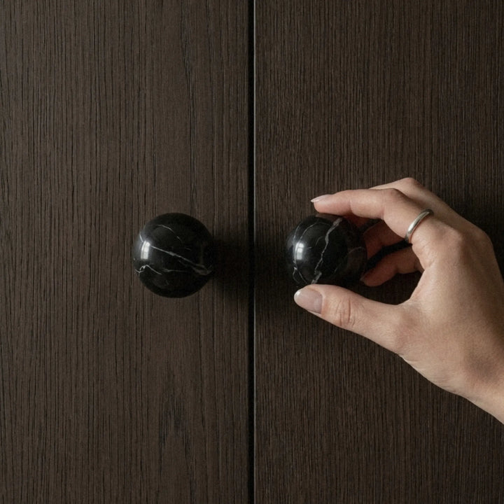 Hand opening dark wood cabinet door with black marble knob, natural stone cabinet hardware detail.