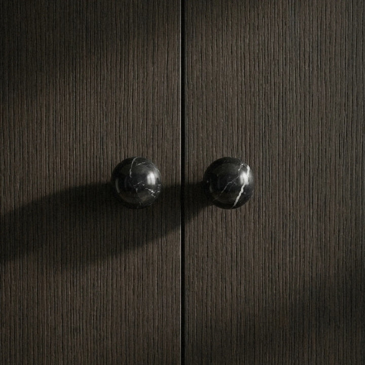 Matte black stone cupboard knobs on dark textured wood cabinet doors for modern kitchens.