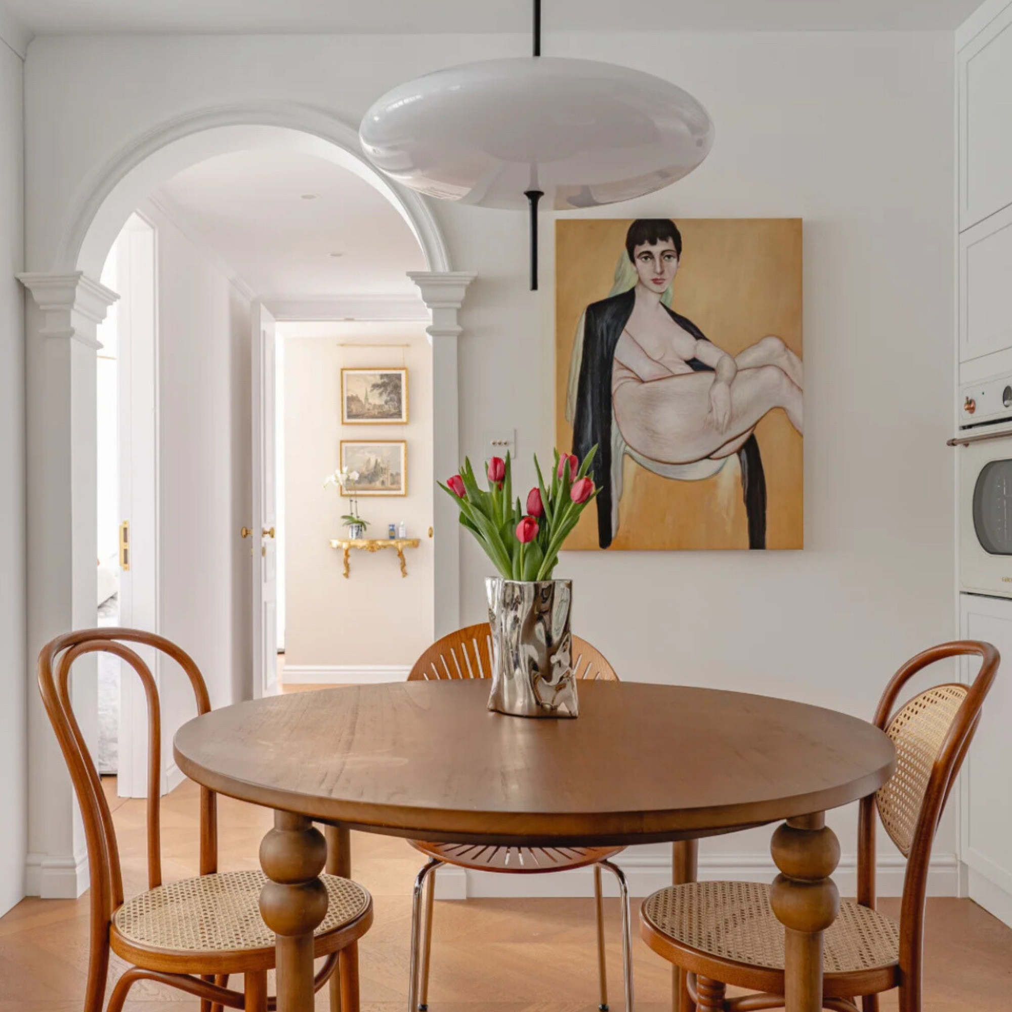 A metallic silver vase with tulips on a cozy wooden dining table in a classic dining area.