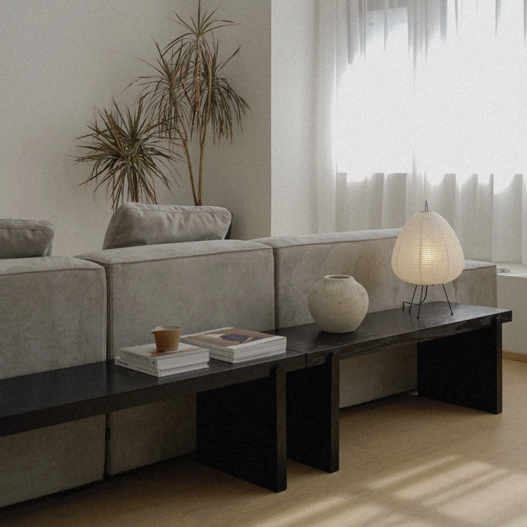minimal washi paper lamp positioned on a dark table beside a sofa and decorative objects.