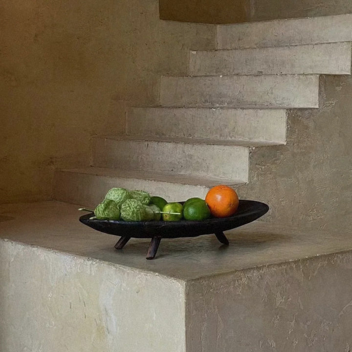 wood fruit bowl resting on a stone surface with fresh fruit arranged inside.
