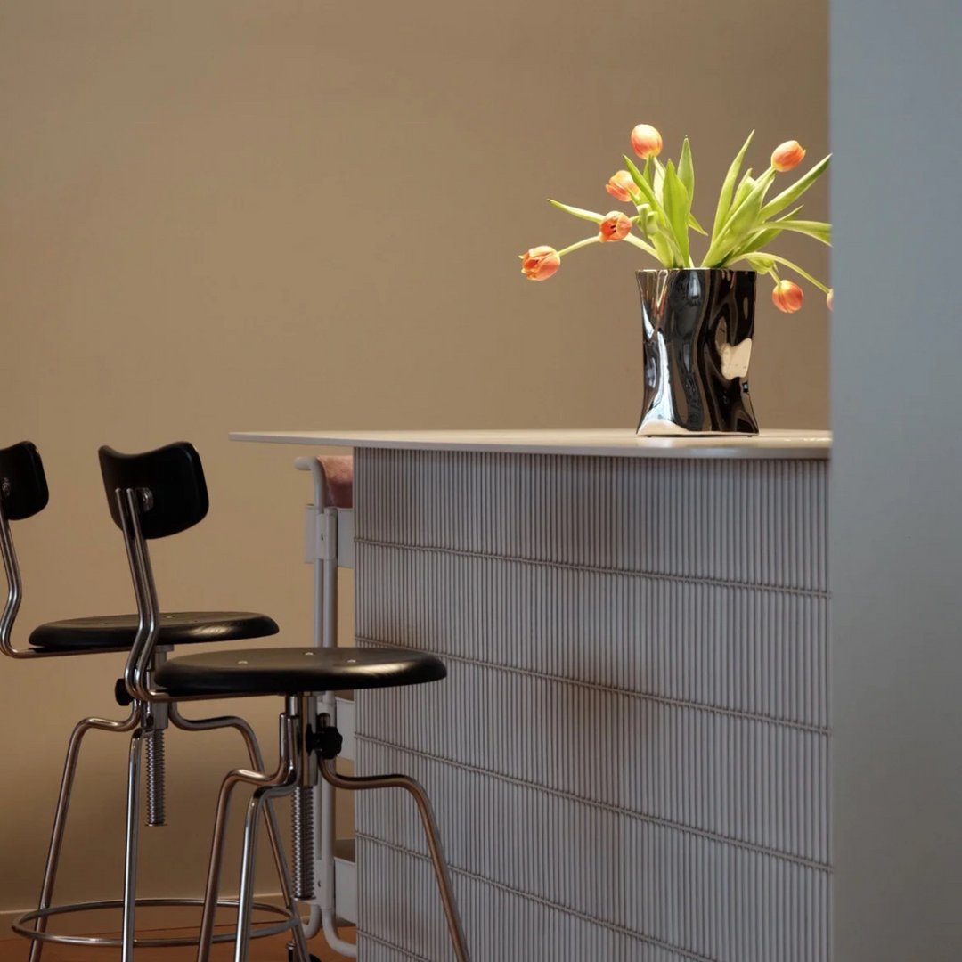 A minimalist bar counter with a metallic silver vase holding orange tulips, enhancing the space with modern elegance.