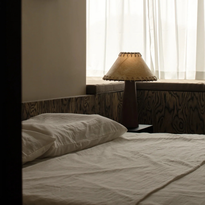 Minimalist bedroom with wooden panel decor, warm table lamp, and soft bedding in neutral tones