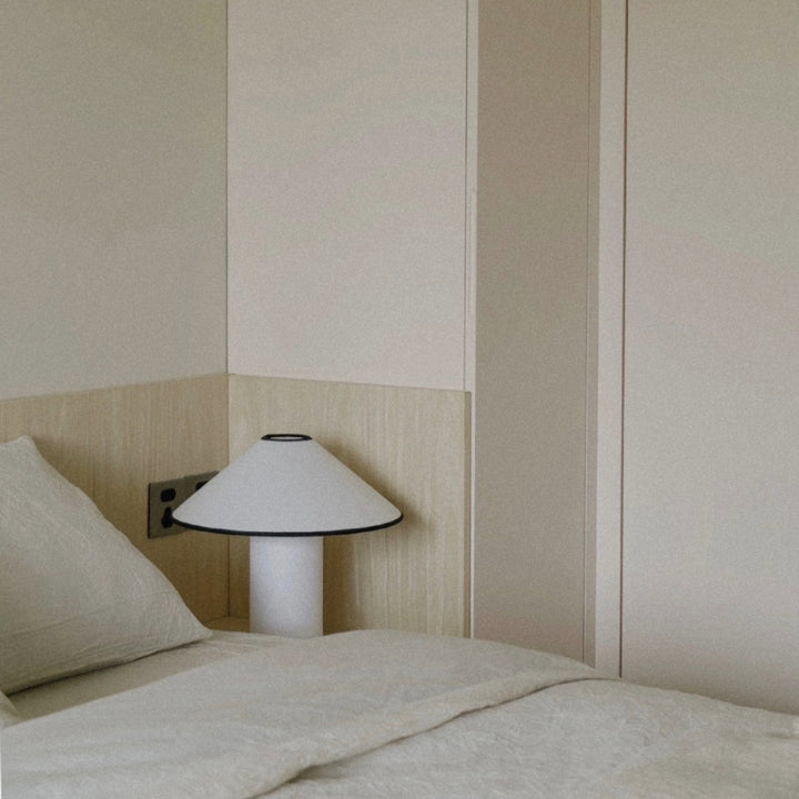 minimalist bedside lamp positioned next to soft bedding in a calm bedroom.