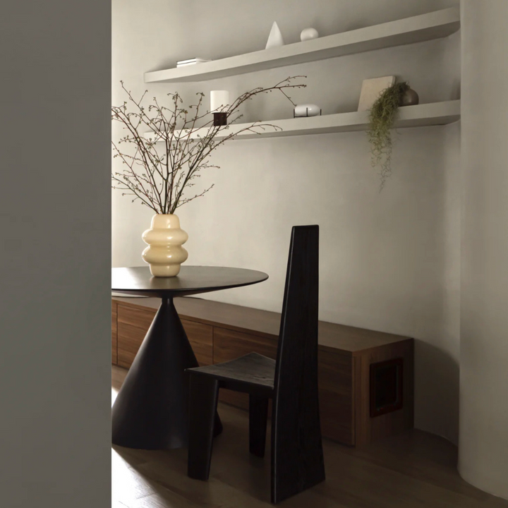 Minimalist dining area showcasing a unique chair design and an elegant vase on a round table.