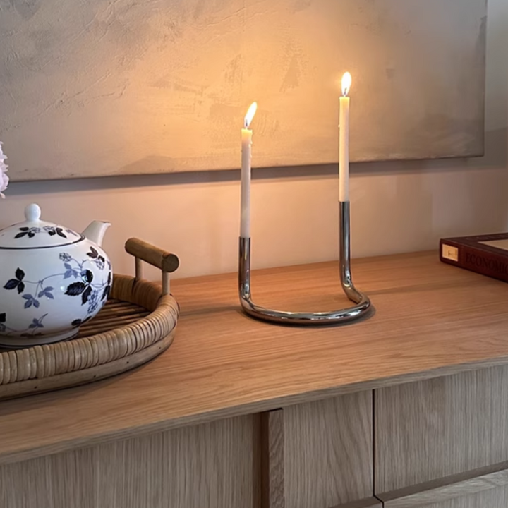 Minimalist polished stainless steel candlestick on a wooden cabinet, perfect for modern interiors.