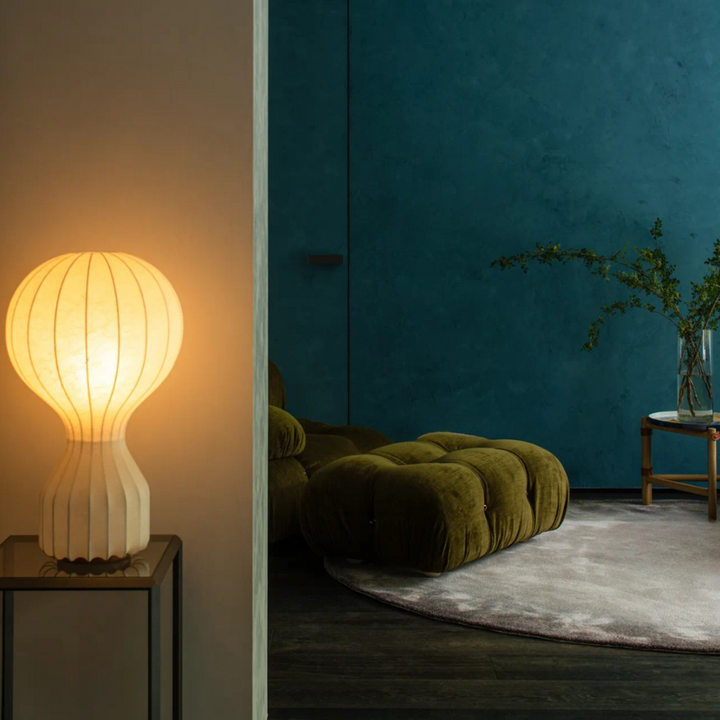 Soft-glow sculptural table lamp lighting a minimalist corner with blue velvet tones.