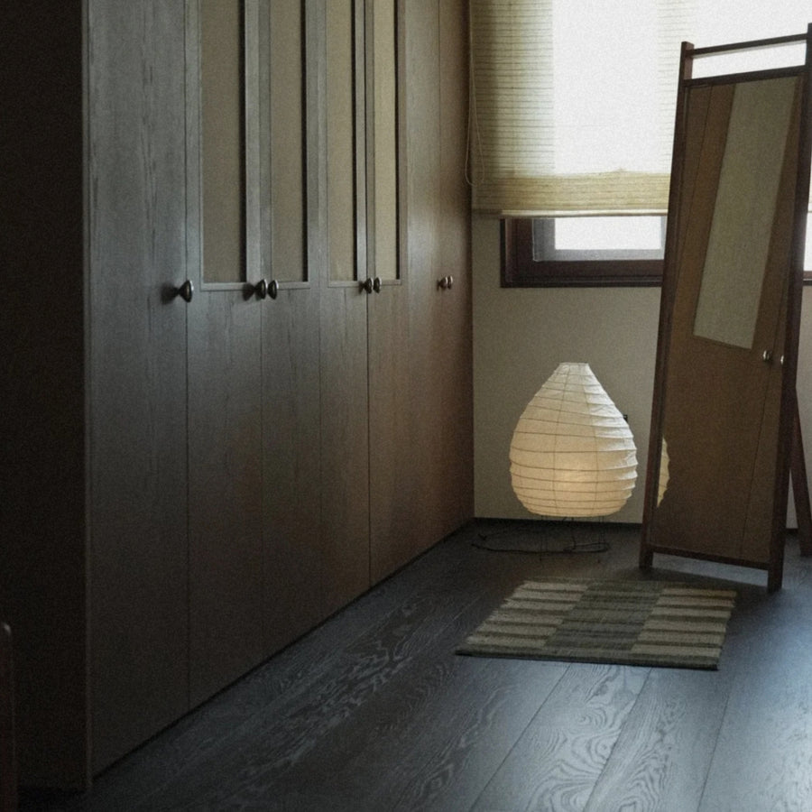 minimalist washi paper floor lamp glowing softly in a hallway corner near wooden cabinetry.