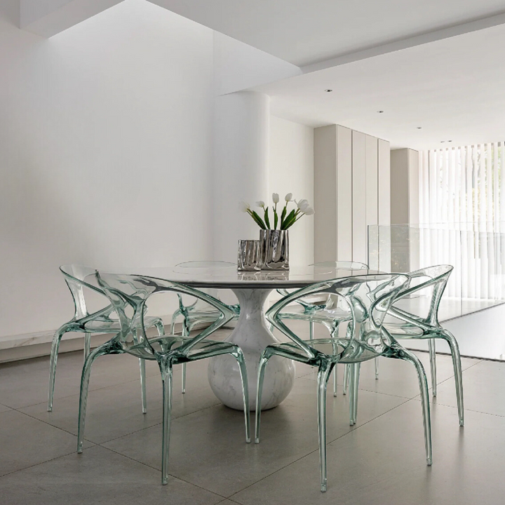 Minimalistic dining room featuring a reflective silver vase with flowers, complemented by glass furniture.