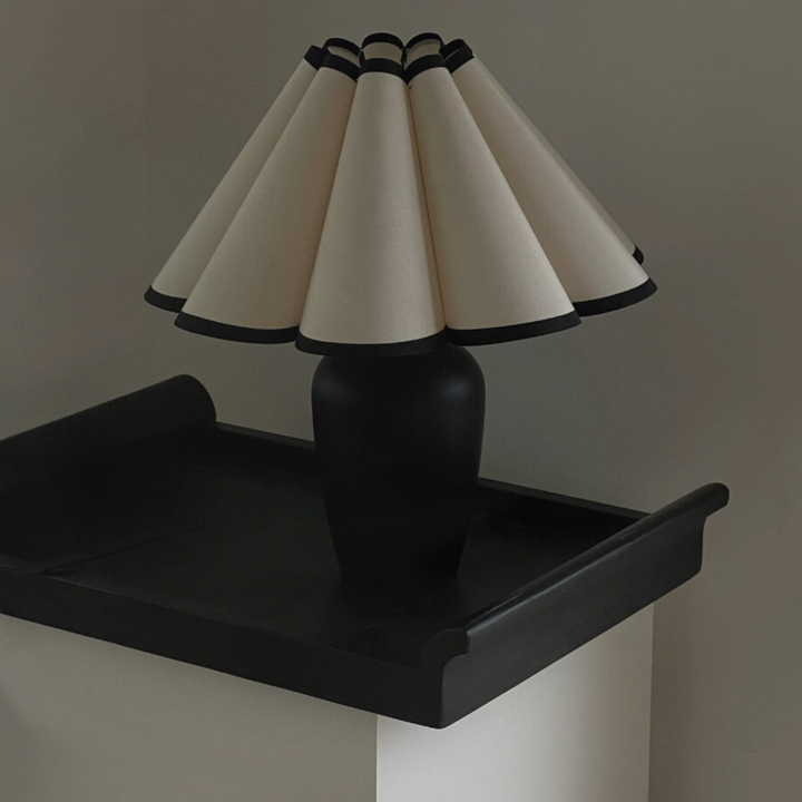 Black table lamp with a cream scalloped shade displayed on a black tray, ideal for adding character to minimalist interiors.