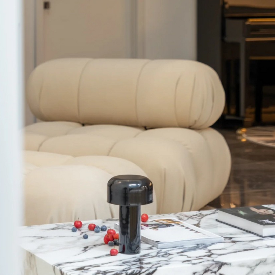 A glossy black mushroom lamp adds a sleek touch to a luxurious marble coffee table surrounded by beige furniture.