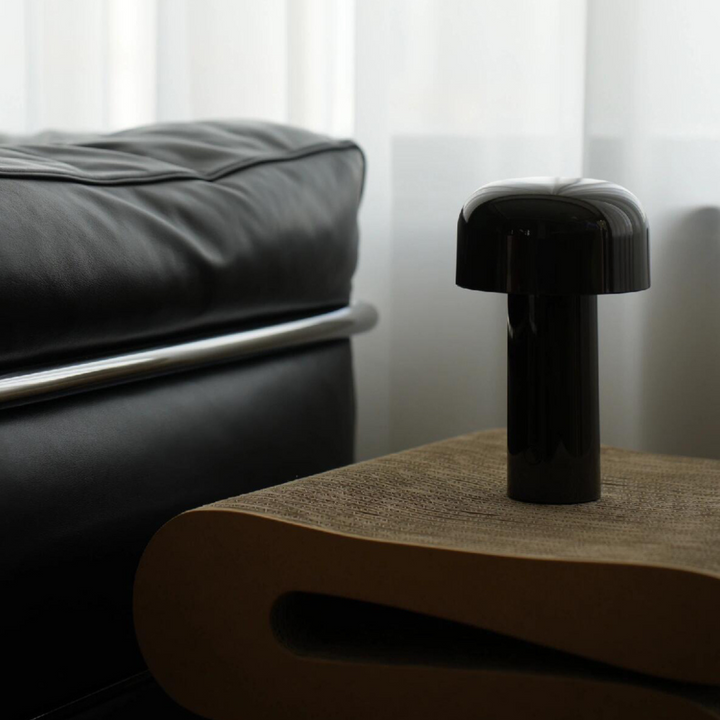 A sleek black cordless lamp on a minimalist wooden side table, placed next to a modern black sofa with clean lines.