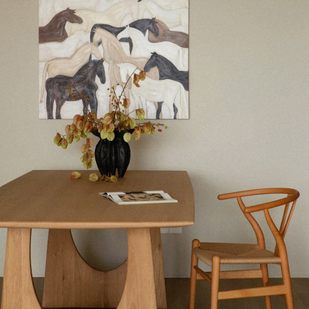 modern black ceramic vase arranged on a dining table beneath wall artwork.