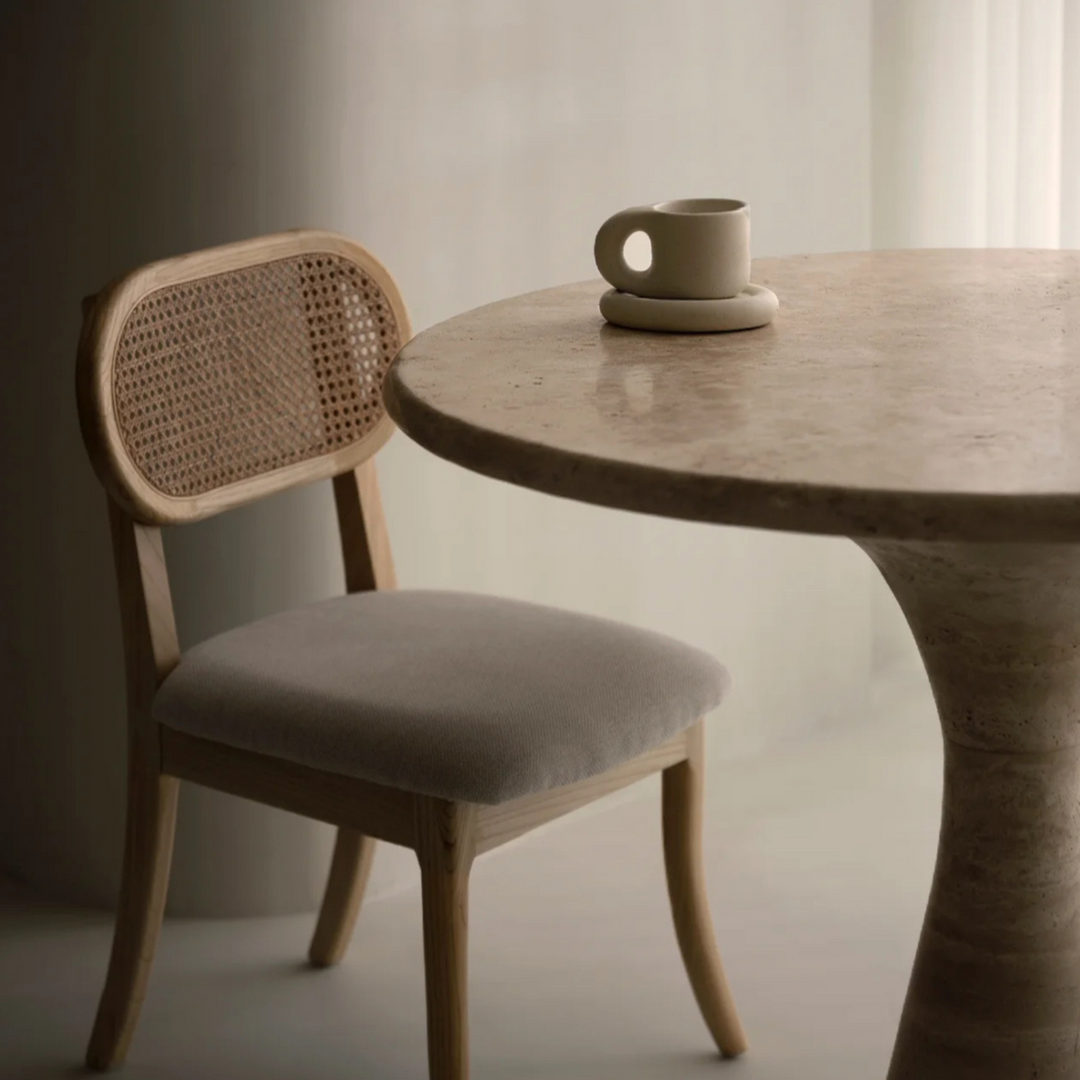 Modern chunky ceramic mug with a matching plate next to a cane chair on a round dining table.