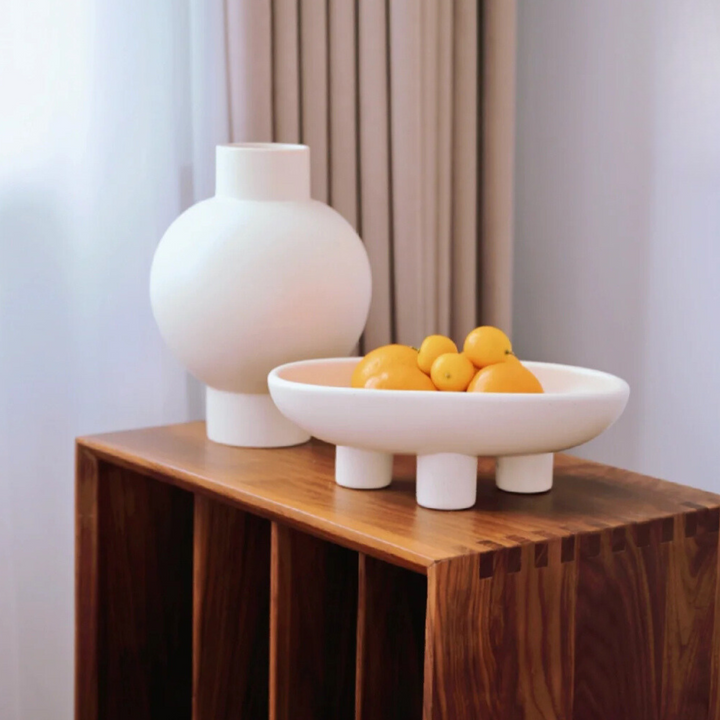 Bold ceramic bowl with a modern design, featuring raised legs on a wooden sideboard. A minimalist addition for clean interiors.