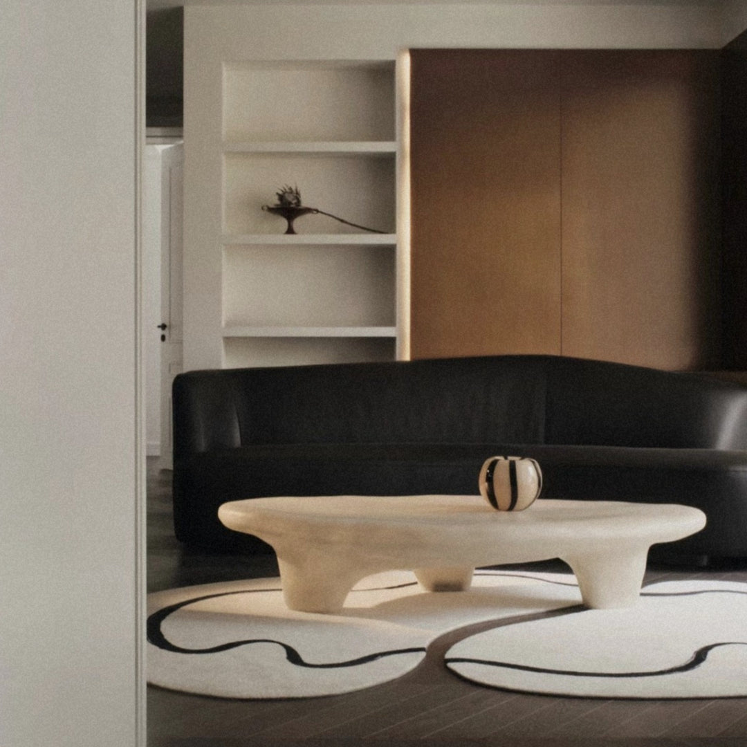 a modern glass vase displayed on a sculptural coffee table in a contemporary living room setting.