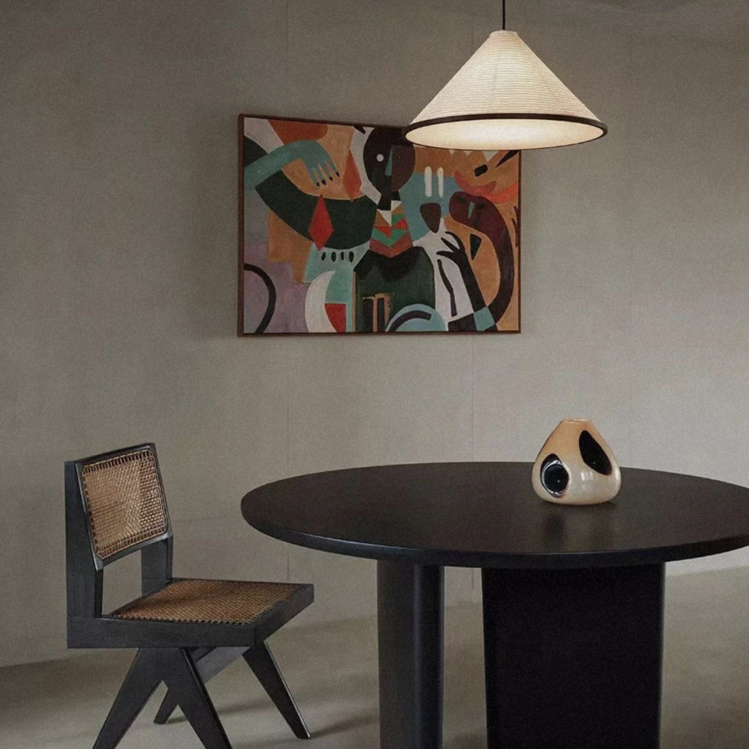 a glass vase sits at the center of a round dining table beneath a pendant light in a modern interior.