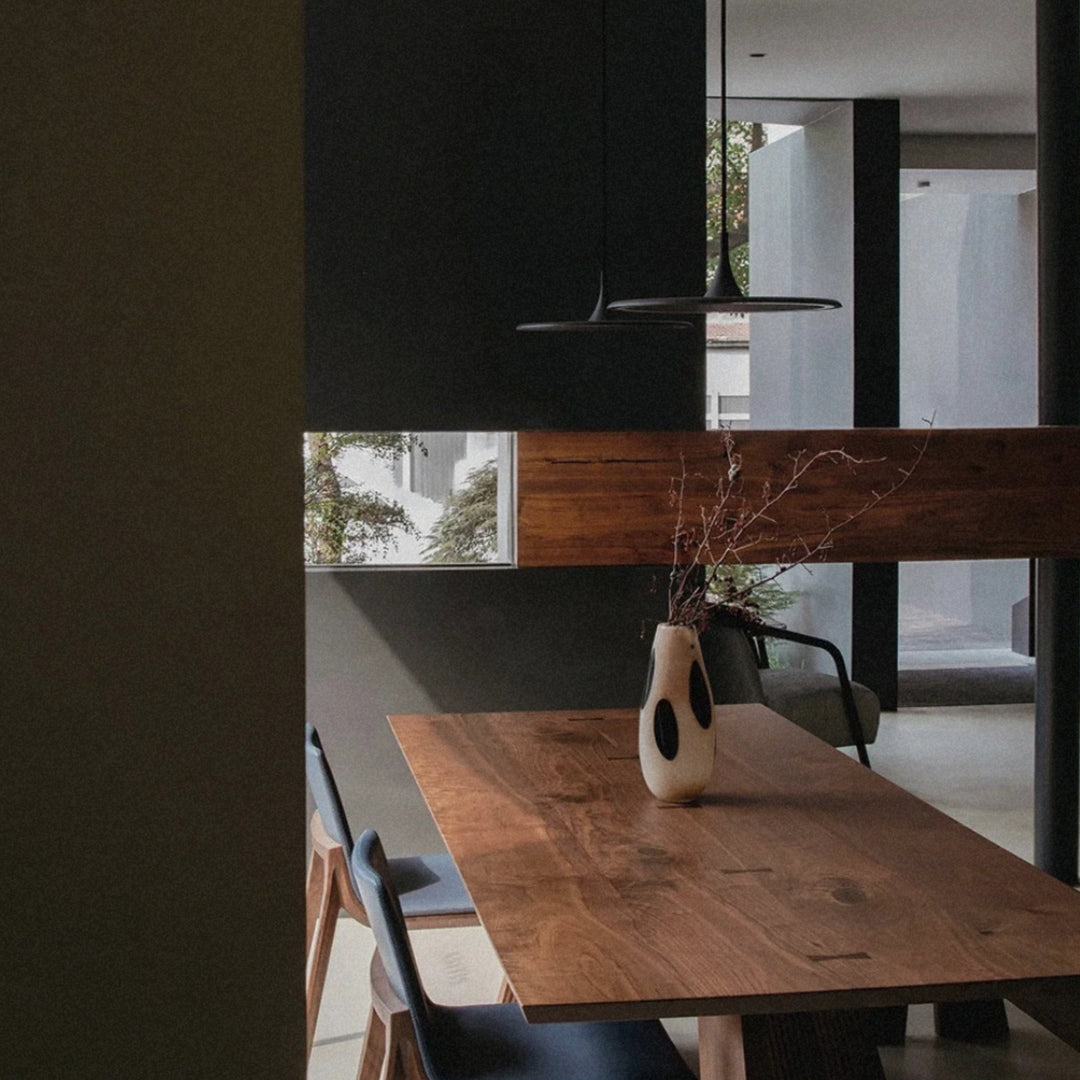 glass vase holding branches placed on a wooden dining table in a contemporary interior.