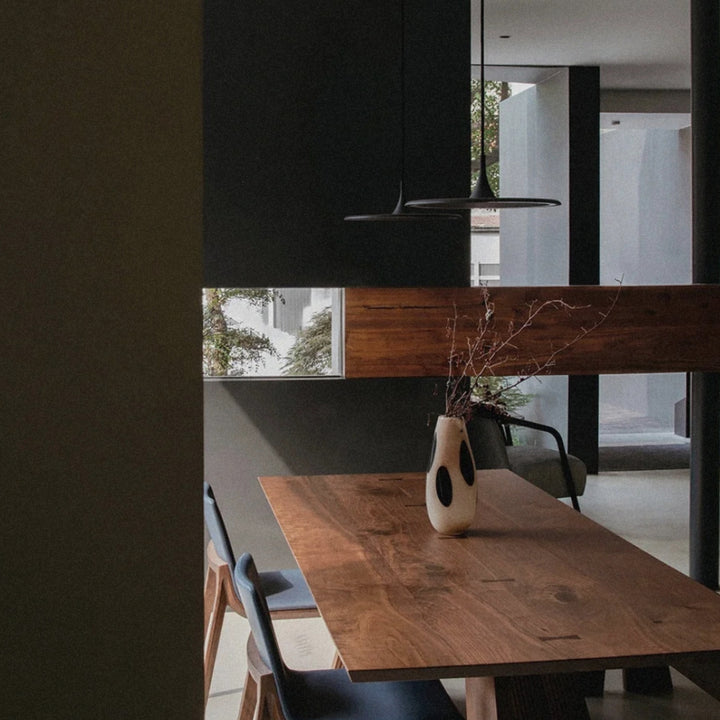 glass vase holding branches placed on a wooden dining table in a contemporary interior.