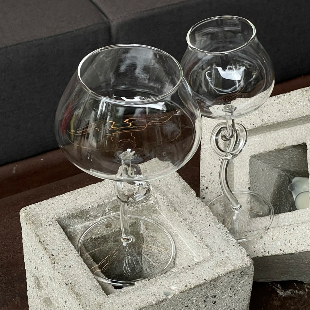 Modern and stylish wine glasses with a unique twist design, placed on concrete blocks for a minimalist, industrial decor look.