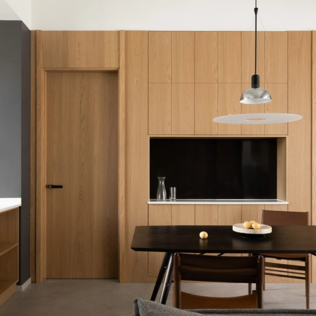 Modern kitchen with chrome pendant light, black accent wall, and light wood cabinetry