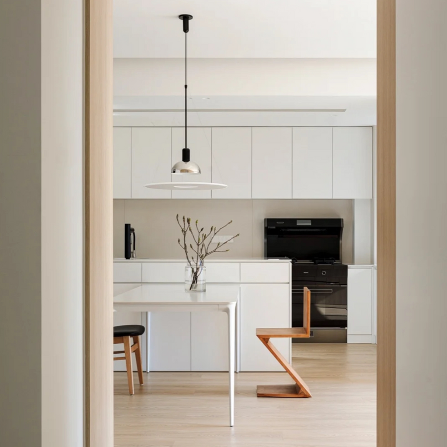 Modern minimalist kitchen with chrome pendant light, white table, and wood cabinetry