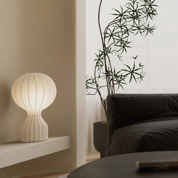 ribbed table lamp casting a soft ambient glow on a shelf beside a sofa.