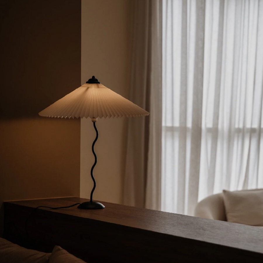 Sleek table lamp with pleated shade casting a warm glow on a wooden surface, adding modern charm to the living space.