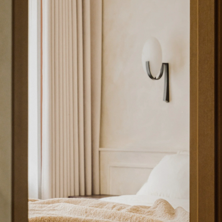 Minimalist marble wall lamp in a neutral bedroom, highlighting timeless French-inspired design.