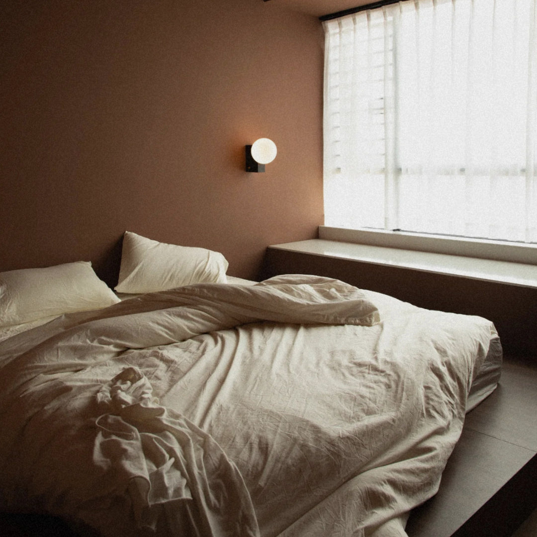 modern wall sconce with opal glass globe installed beside a bed.