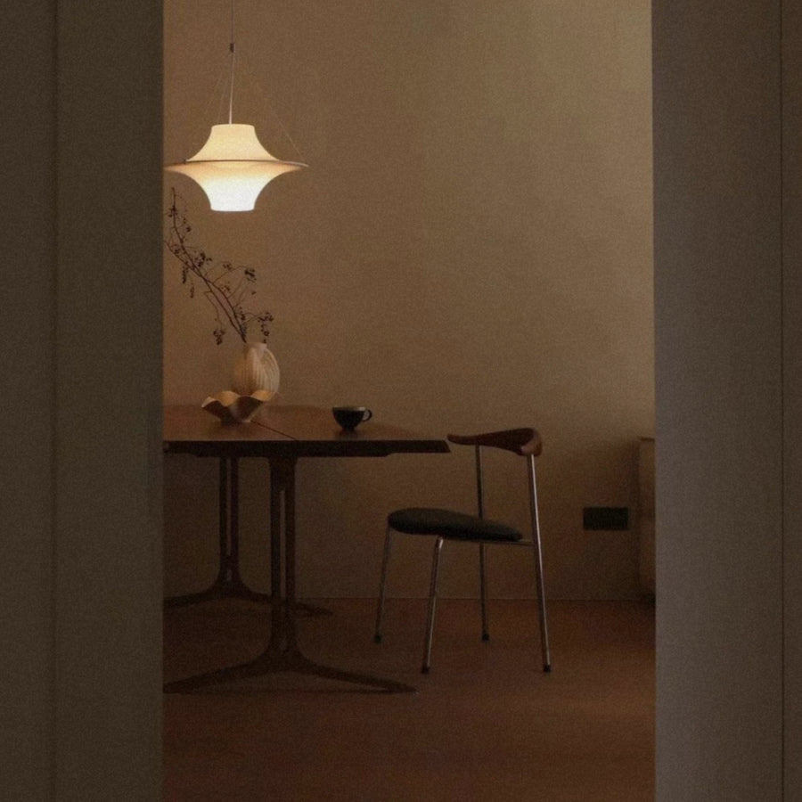 modern white pendant light casting a warm ambient glow above a small dining table in a calm minimalist interior.