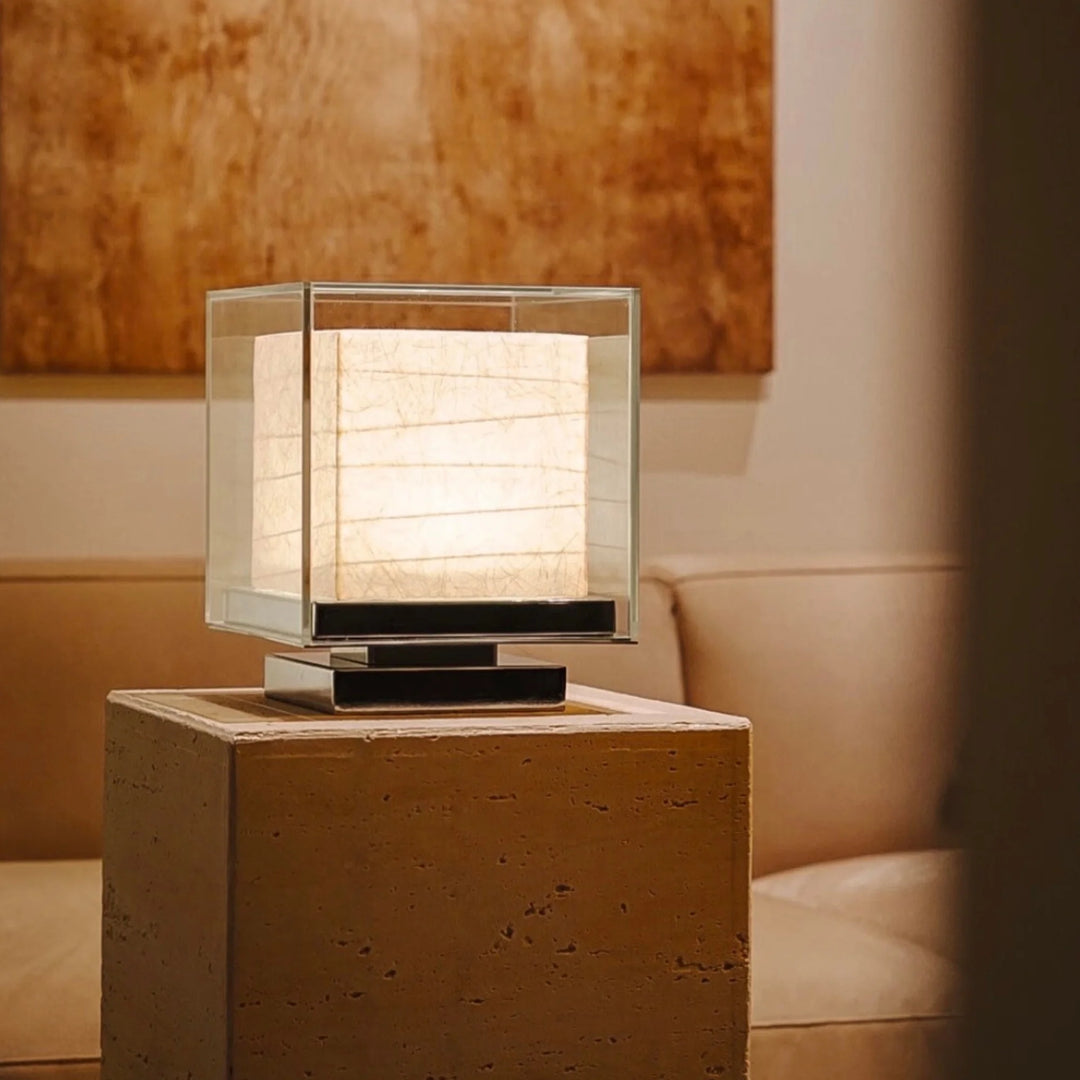 Wireless Nara lamp glowing softly on a travertine block beside a sofa.