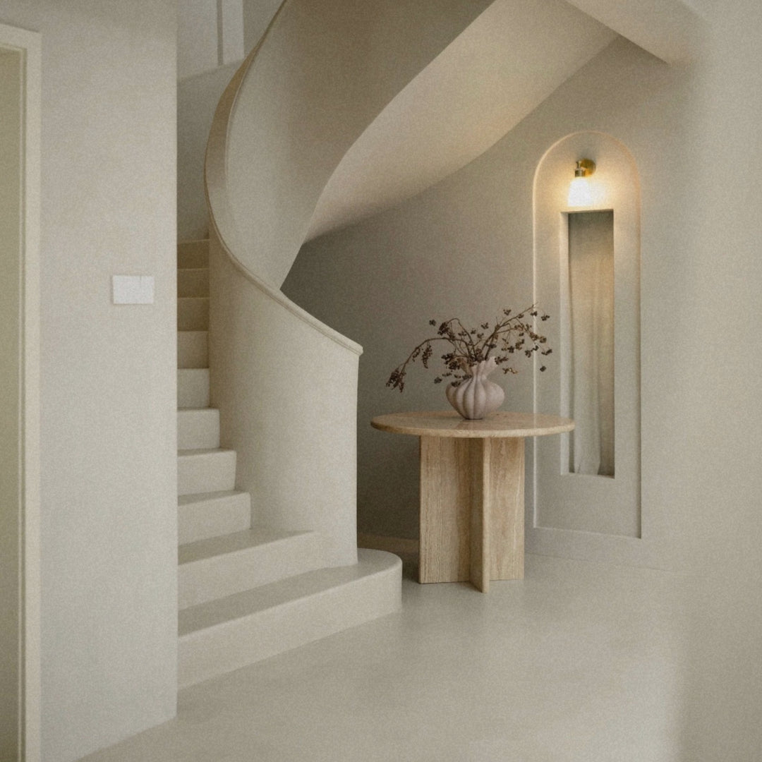 neutral sculptural ceramic vase placed on a stone table in a minimalist entryway interior.