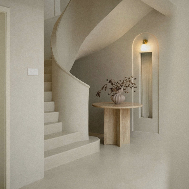 neutral sculptural ceramic vase placed on a stone table in a minimalist entryway interior.