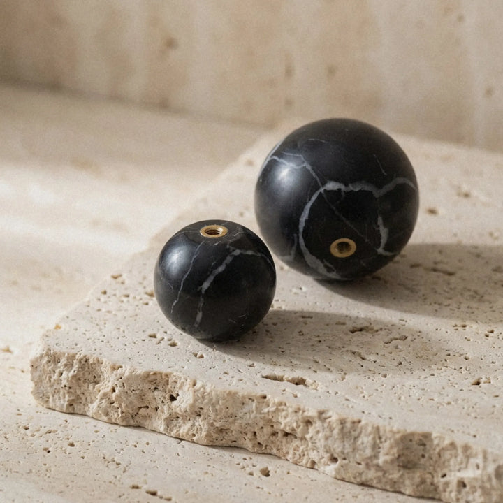 Black marble cabinet knobs resting on travertine surface, sculptural stone hardware for organic modern interiors.