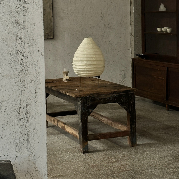 Organic modern paper floor lamp placed against a textured wall and rustic wooden table in a soft lighting scene.