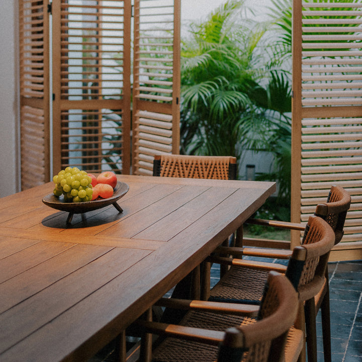 wooden serving bowl with fruit set on an outdoor dining table surrounded by chairs.