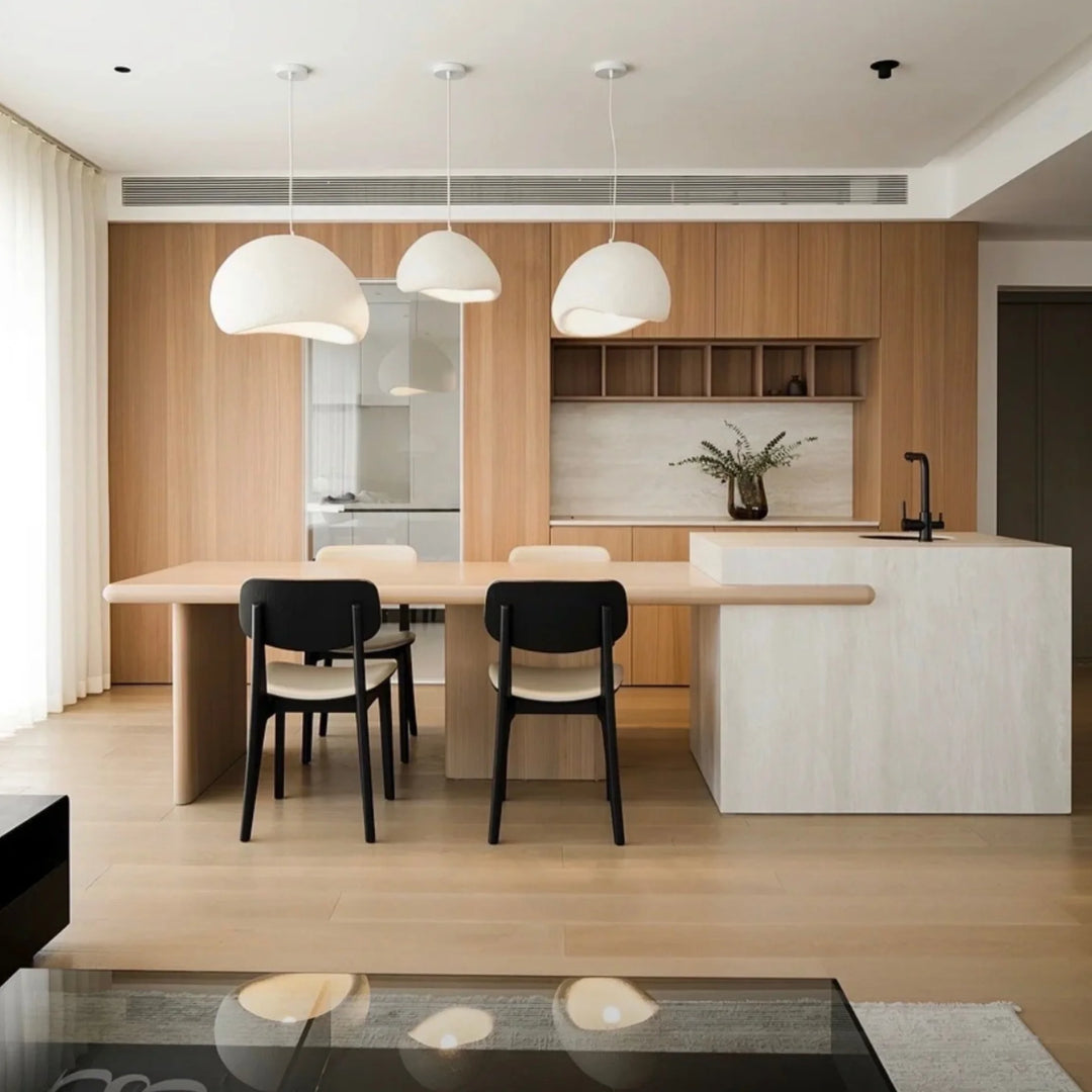 Three Oxi pendant lights in different sizes above a dining island with soft wood tones.