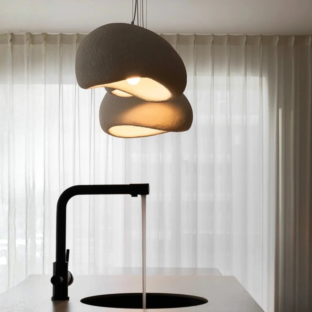 Two sculptural Oxi pendant lights softly glowing above a modern sink and sheer curtains.