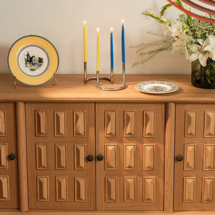 Polished stainless steel candle holder with colorful candles on a vintage-style cabinet.