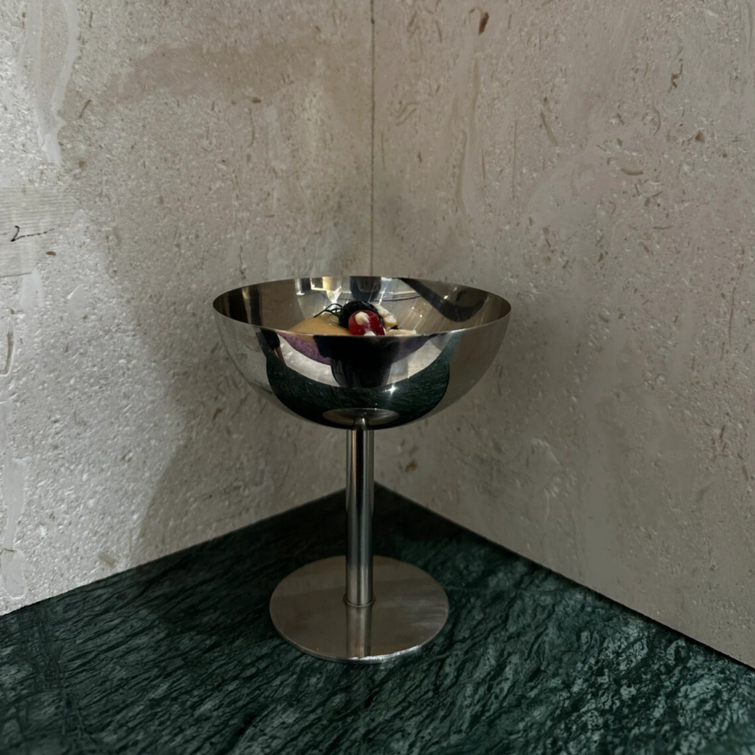 Polished stainless steel coupe on a marble table, offering a bold and elegant centerpiece for modern interiors.