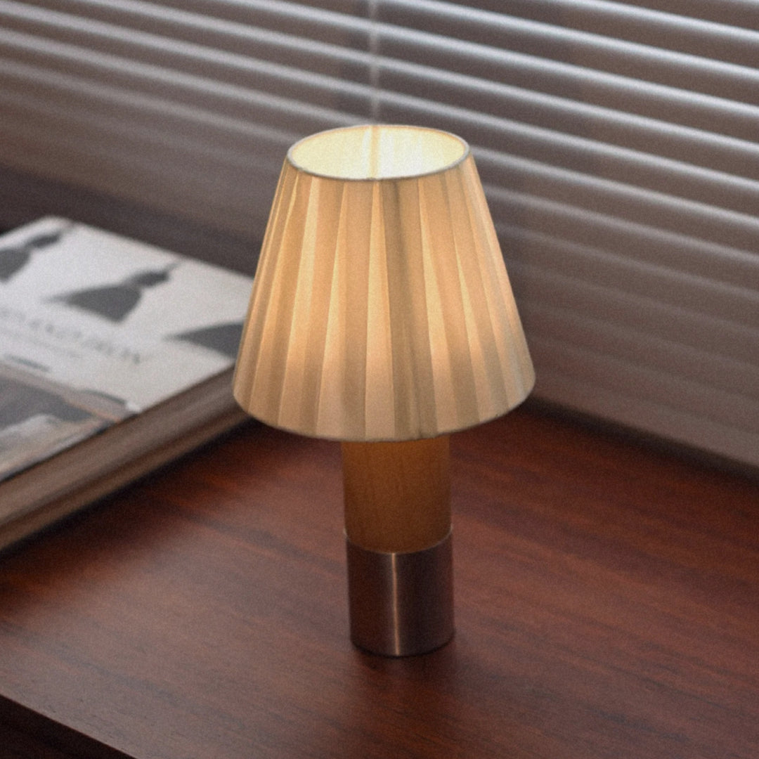 portable table lamp with a pleated shade placed on a wooden surface near window blinds.