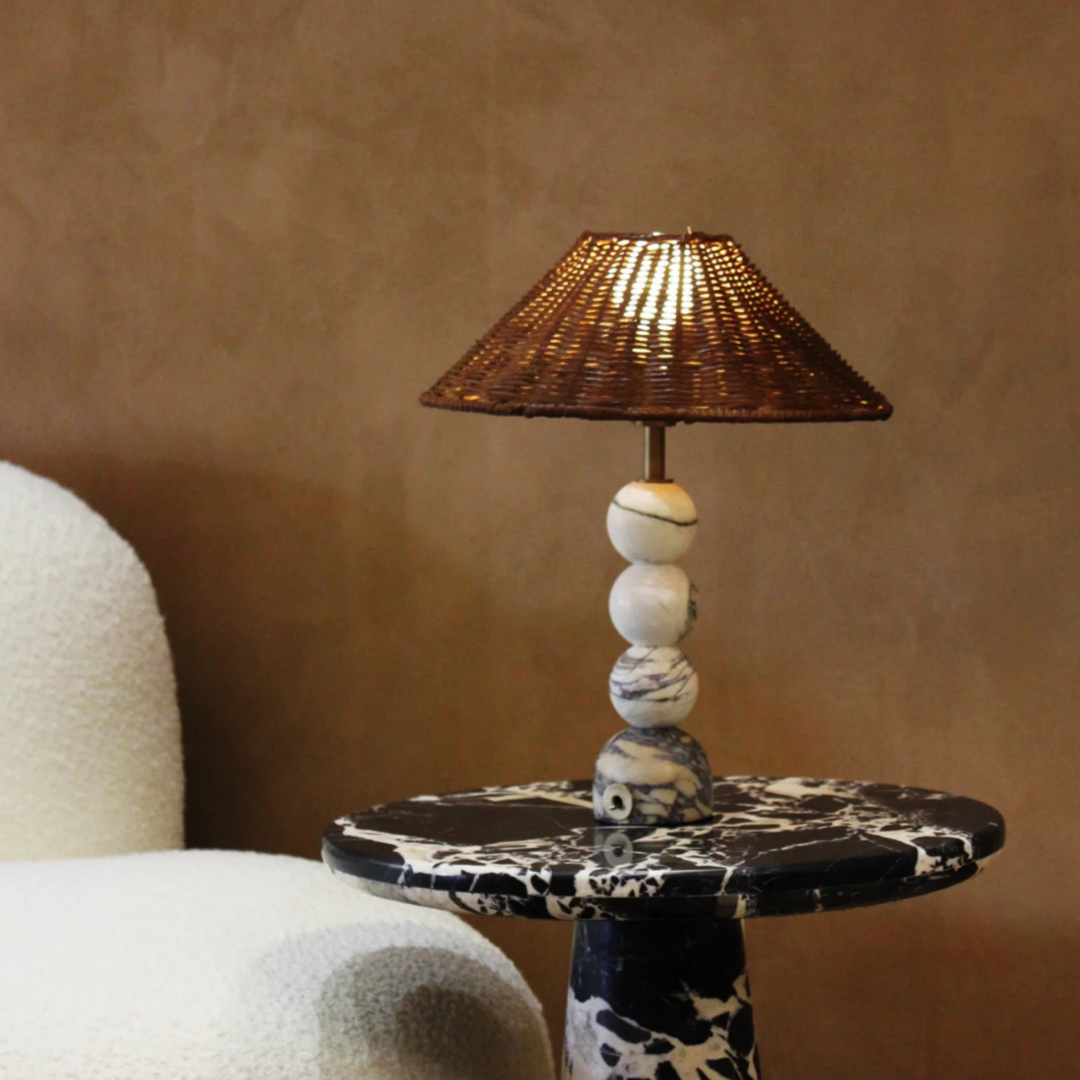 Rattan lampshade with a marble base on a black side table, styled in a cozy modern corner.