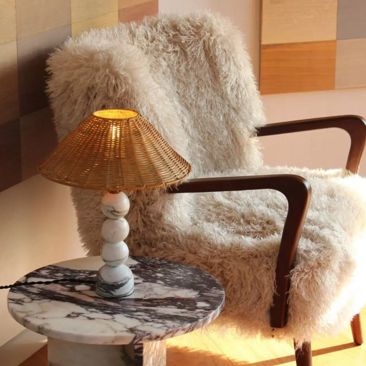 Rattan and marble lamp on a monochrome table next to a sheepskin-covered accent chair.